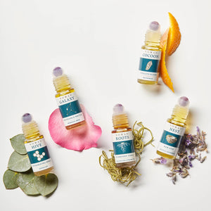Nomad Botanicals Carry-on Wellness Collection, including five different aromatherapy blends: Hive, Galaxy, Roots, Cocoon, and Nest. Image includes botanicals next to each product (Hive with Eucalyptus; Rose with Galaxy; Moss with Roots; Orange Slices with Cocoon; Lavender with Nest).