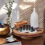 Picture of Aroma Journey 2 Collection with 5 essential oil blends in Cinnamon Box on platter with black Ultrasonic Ceramic Diffuser in living room